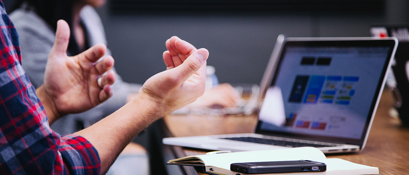 A person sitting at a desk with a laptop, making hand gestures.