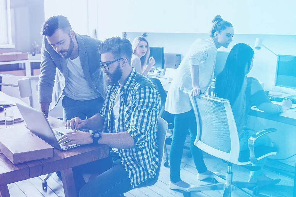 A collective of professional individuals collaborating on laptops and computers in a modern office setting.