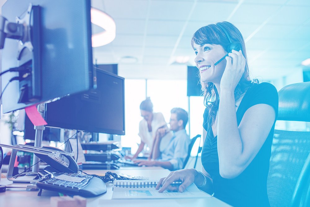 A female professional using a telephone while seated at a computer desk, engaged in a phone call.